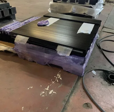 Stack of black powder-coated slatted metal panels wrapped for handling
